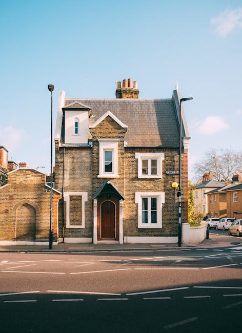 Exterior view of a traditional brick residential building on Finchley Road near Swiss Cottage, with a pitched tiled roof, white-framed sash windows, and a brown front door. The building is situated on a paved street with a sidewalk, and adjacent houses can be seen in the background. The scene is well-lit by natural daylight, highlighting the clean and maintained façade. Swiss Cottage Cleaners provides professional domestic cleaning services to keep such homes pristine, emphasizing surface cleaning, sanitisation, and deep cleaning to maintain hygiene and appearance in residential properties near Swiss Cottage, SWISS COTTAGE.